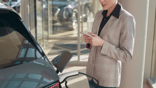 Blonde Frau wartet auf Elektroauto zum Aufladen
