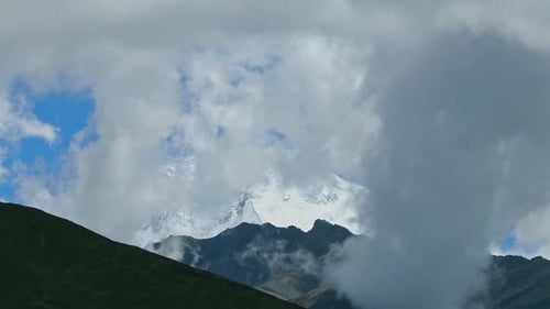 Timelapse Clouds Swirl Over a Mountain Valley a Snowy Peak in the Distance