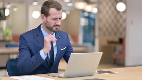 Tired Businessman with Laptop Having Neck Pain in Office