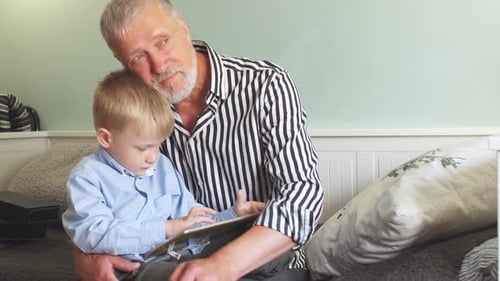 Child and Senior Man Using Tablet Together Indoors