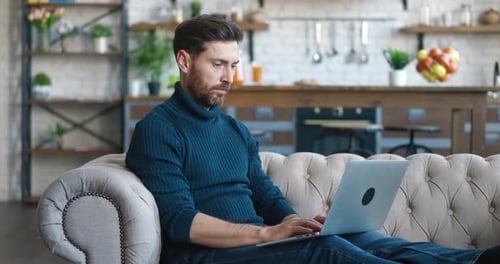 Man using laptop on couch in bright home