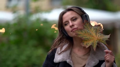 Romantic Woman Is Listening Melody By Wireless Headphones on Street in City at Autumn Day, Playing