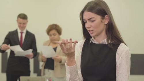 Portrait of Angry Young Woman in Formal Wear Speaks By Her Cellphone in the Foreground in the Office