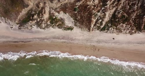 Blick von oben nach unten auf Wellen, die im Sand brechen und über tropischen Sandstrand und Wellen fliegen
