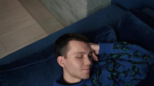 Young Adult Sleeping on Blue Couch Indoors
