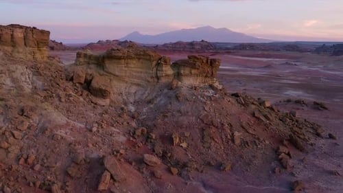 Flying backwards from red rocky hill revealing landscape and mountains