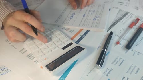 Nahaufnahme einer männlichen Hand, die einige Berechnungen durchführt und sich Notizen im Finanzbericht macht
