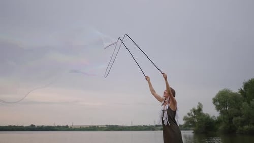 Woman Creates Bubbles on Beach by Lake