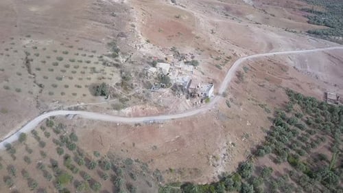 Drone view of a small human settlement in a rugged terrain; road passing through the rocky highlands
