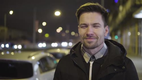 A Young Handsome Man Smiles at the Camera in a Street in an Urban Area at Night - Closeup
