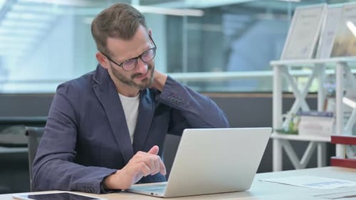 Middle Aged Businessman Having Neck Pain While Using Laptop in Office