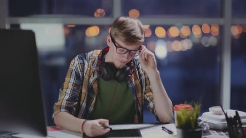 Young Designer Works in Empty Office at a Later Time, Feels Tired