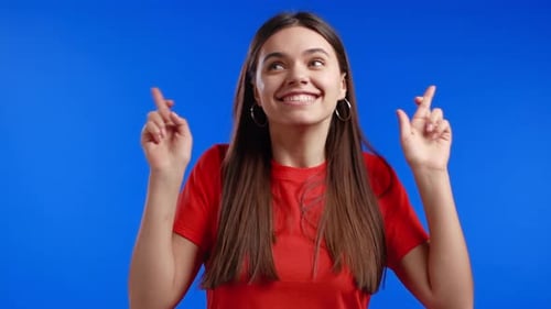 Smiling Woman with Fingers Crossed against Blue Background