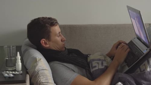 Man Lies on Couch Using Laptop Near Medicine