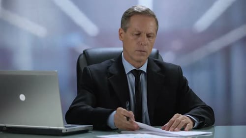 Attentive Company Boss Reading and Signing Documents at Office Table With Laptop