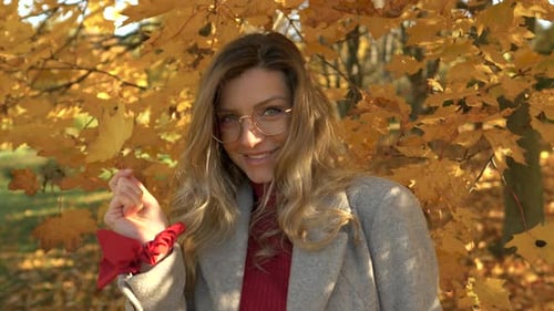 blond woman smiles and plays with yellow and golden leaf in autumn park