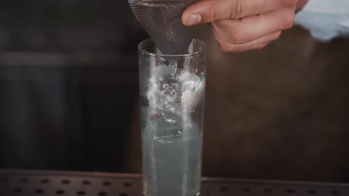 Pouring Liquid Through Strainer into Glass of Ice