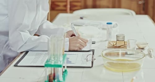Frau in einem Chemielabor schreibt Notizen zu ihren Experimenten mit Reagenzgläsern in einem Rack