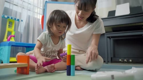 Asiatische glückliche Familie, schöne Mutter und kleines Mädchen spielen zusammen Spielzeug im heimischen Wohnzimmer