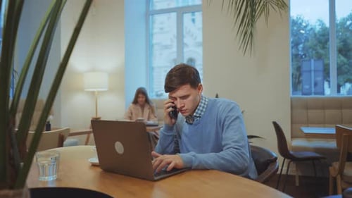 Businessman Talking on Phone and Using Laptop in Cafe