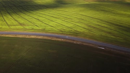 Top View of a Car Driving Along a Rural Road Between Two Fields