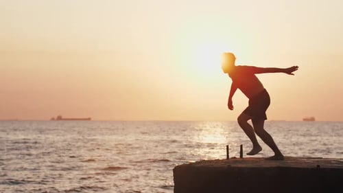 Junger Mann springt vom Sea Pier und macht Backflip bei schönem Sonnenaufgang Super Zeitlupe