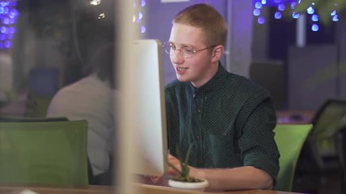 Young Emotional Man in Glasses Sitting at His Workplace in Front of Modern Computer