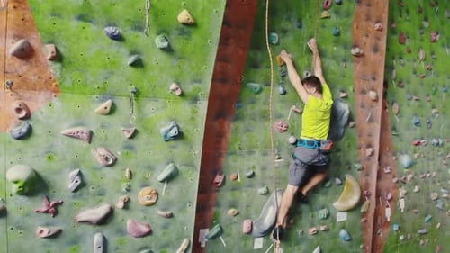 Male Climber Climbs the Cliff Wall in the Room Reaching and Gripping Hold