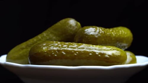 Pimply pickled cucumbers close-up on a white plate on a black background