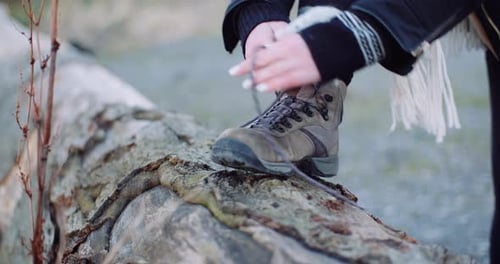 Person Tying Hiking Boot on Tree Trunk