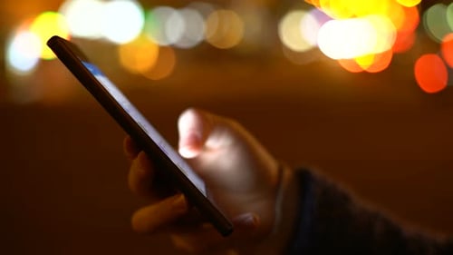 Hands Using Smartphone at Night with Bokeh Lights