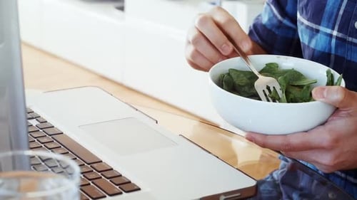 Man Eating Salad While Using Laptop