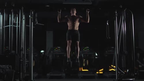 Athletic Man führt Klimmzüge an der Horizontalstange durch Krafttraining im Fitnessstudio Filmmusik Light