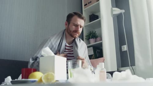 Un homme malade atteint de grippe assis sur un canapé à la maison. Ill jeune homme avec froid vérifier la température avec