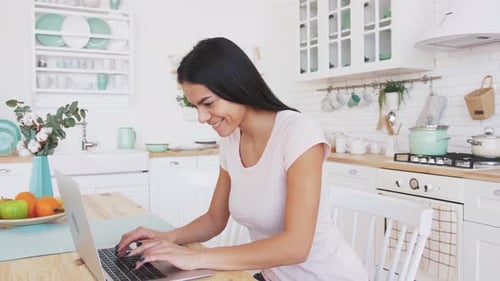 Smiling Woman Working on Laptop in Bright Kitchen