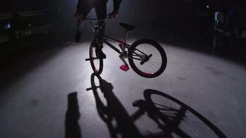 BMX rider doing tricks in dark warehouse.