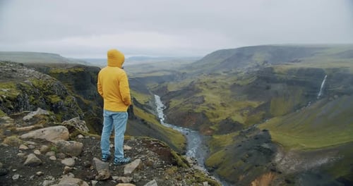 Man in Yellow Coat on Cliff Edge with Haifoss Waterfall in Background