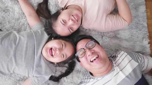 Top view of happy Asian family lying, looking at camera and laughing together