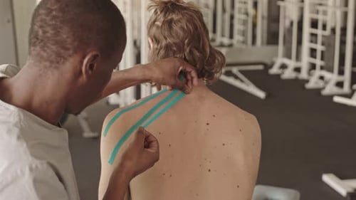 Applying Therapeutic Tape to Man's Shoulder for Treatment