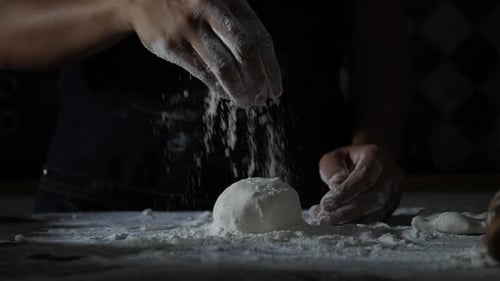 Hands Sprinkle Flour on Dough Ball in Kitchen