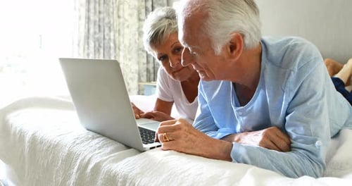 Senior Couple Using Laptop While Lying on Bed