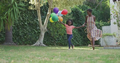 Child and Adult Run with Balloons in Yard