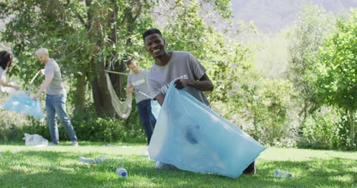 Happy diverse group of friends in volunteer t shirts putting plastic waste in refuse sacks outdoors