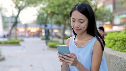 Young Woman Using Mobile Phone in City Park