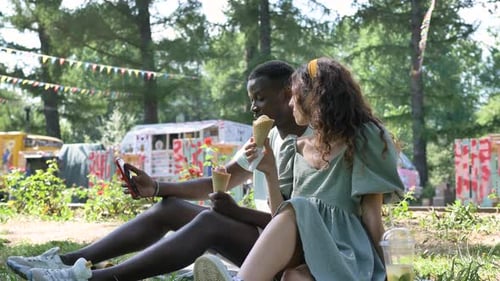 Different Races Couple Sits on Park Grass Eating Icecream