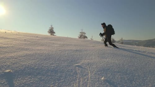 Hiker with Backpack Walking on Snowy Mountain Hillside on Cold Winter Day