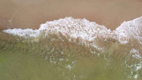 AERIAL: Medium Shot of Top View Shot of Waves Crashing on the Shallow Shore and Spilling on Sand