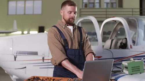 Bearded Mechanic Using Laptop in Hangar