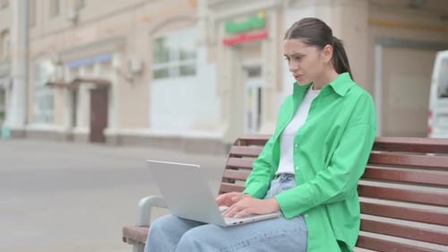 Hispanic Woman Reacting to Loss on Laptop While Sitting Outdoor on Bench