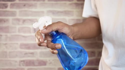Hand Squeezing Blue Spray Bottle Against Brick Wall
